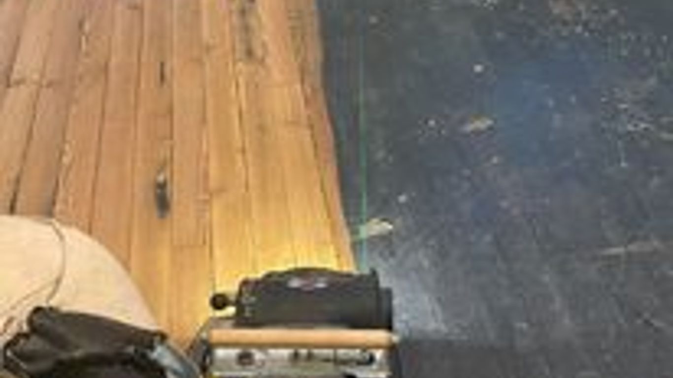 A floor refinishing machine on a partially sanded wooden floor.